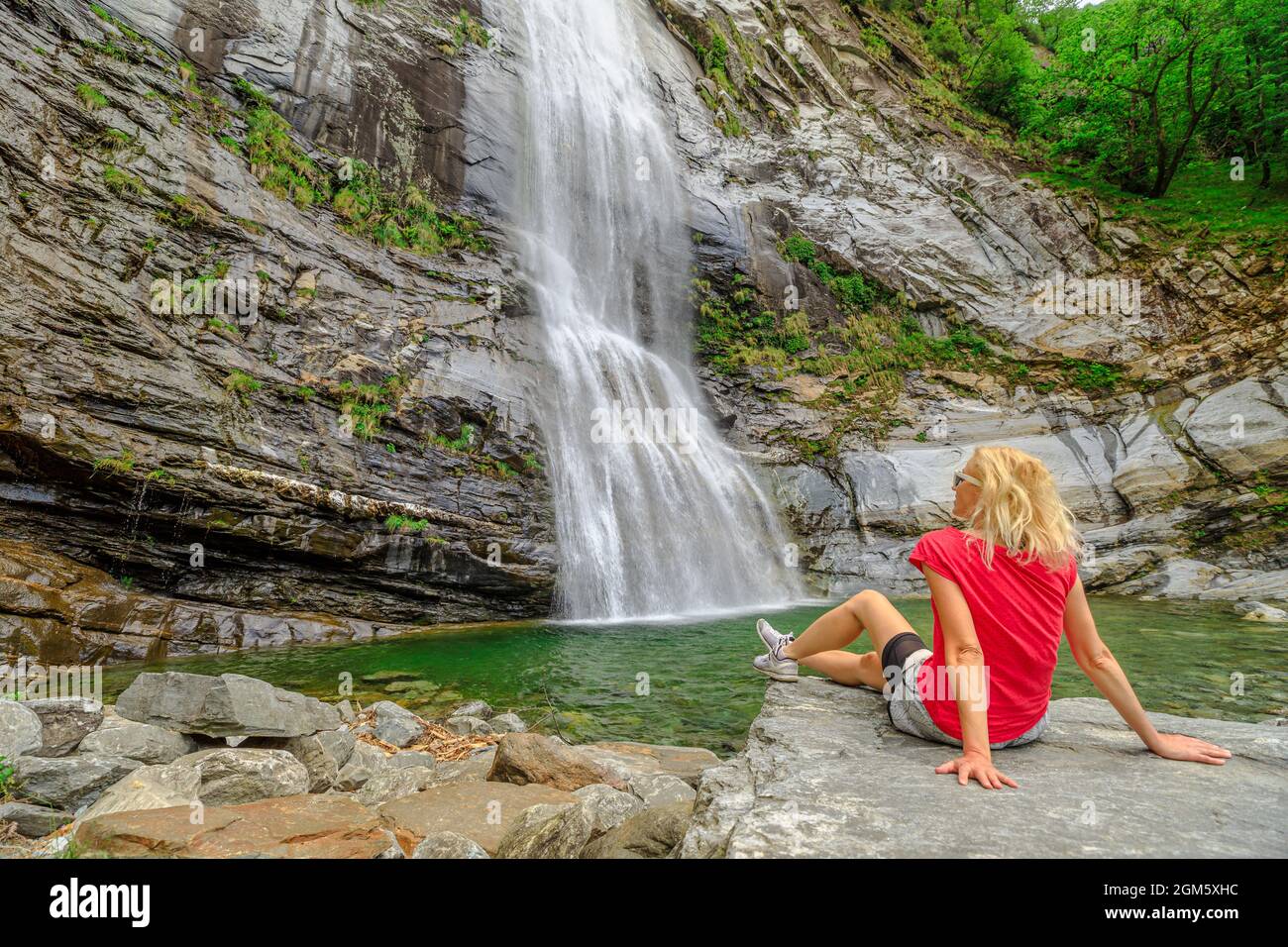Woman sitting by the water of great waterfall of Bignasco, Valle Maggia, intersection point between the Bavona valley and Lavizzara valley, Cevio in Stock Photo