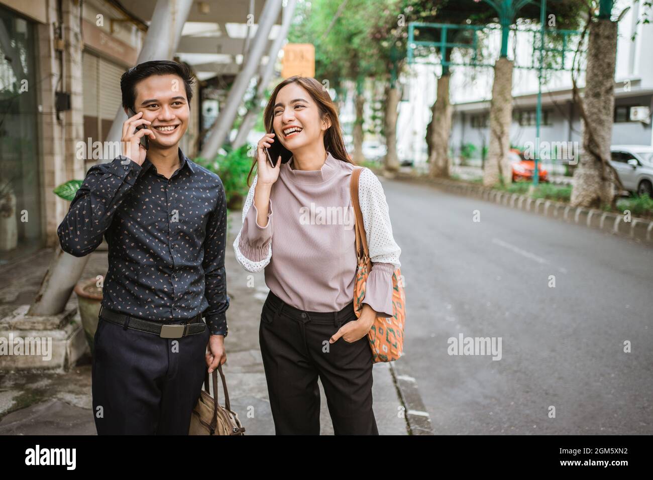 asian man and woman on their phone talking while going to office Stock Photo