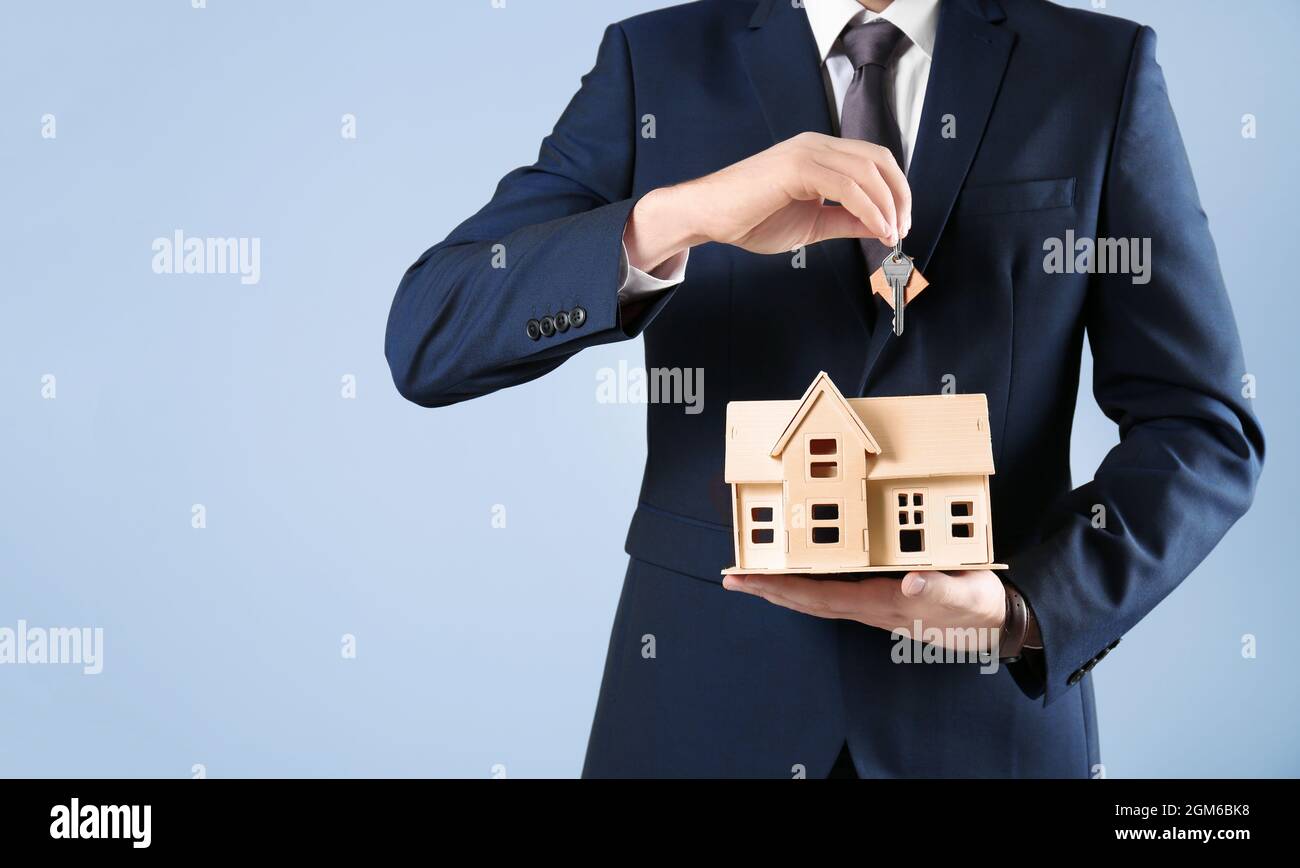 Real estate agent holding house model and key on grey background Stock ...