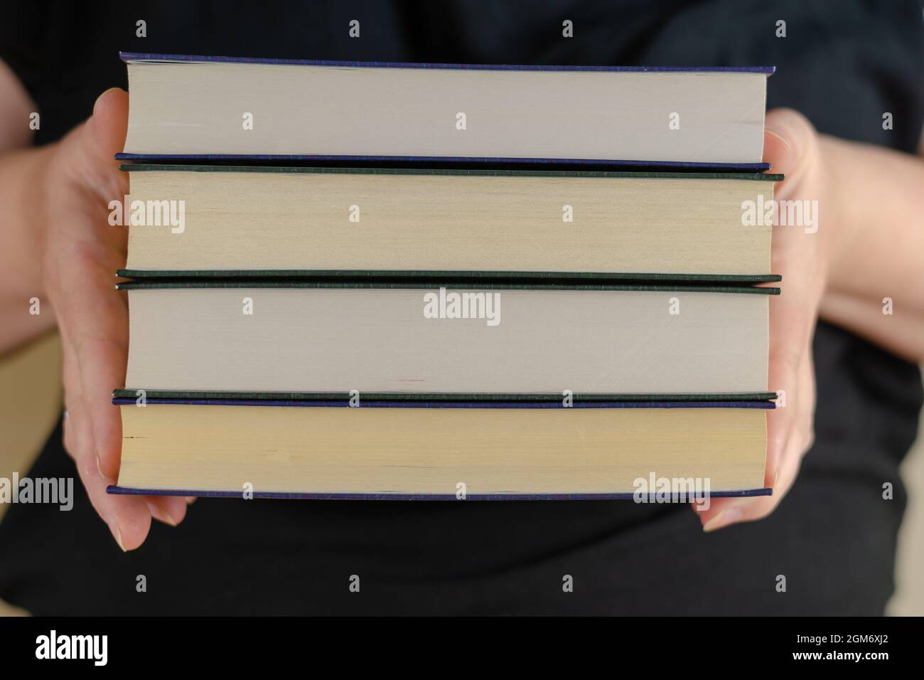 An adult Woman holding a stack of books. Woman's hands with hard Stock Photo