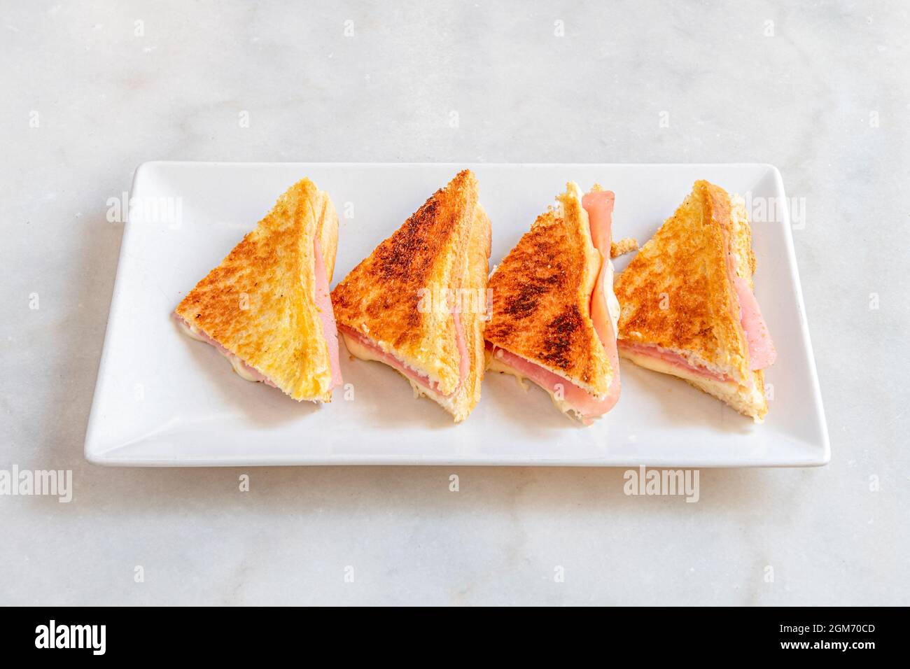 Mixed sandwich of grilled sliced bread with cheese and ham on a white plate. Stock Photo