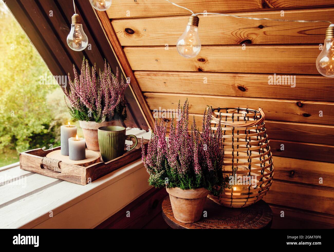 Small natural color wooden cabin balcony with heather flowers, candlelight flame and steaming cup of tea coffee. Cute autumn hygge home decor arrangem Stock Photo