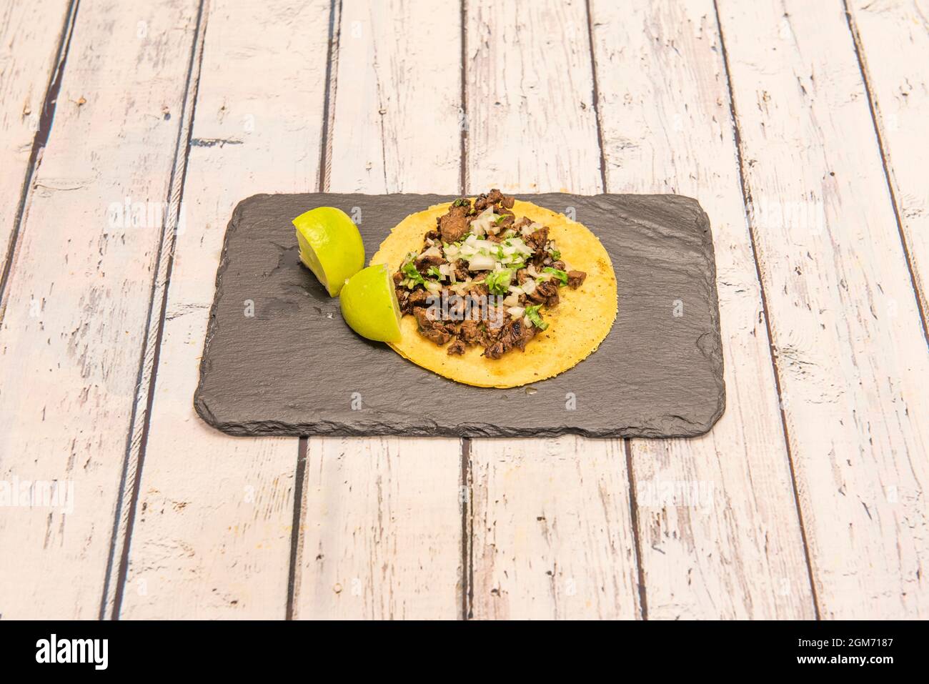 Taco recipe with corn tortilla and flank steak with lime wedges on black slate plate Stock Photo