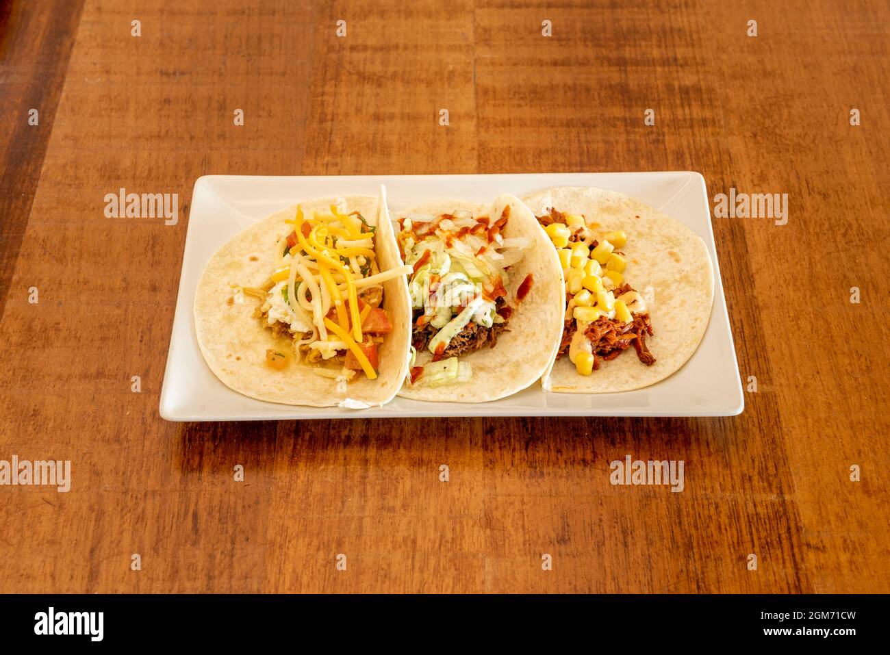 Wheat flour tortilla tacos with assorted fillings, grated cheese, pulled meat, sweet corn on wooden table Stock Photo