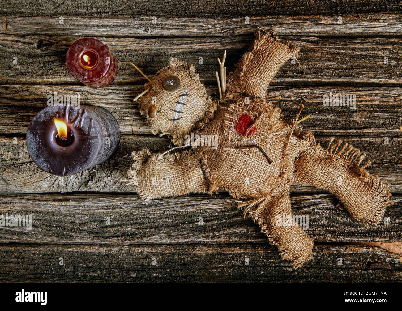 classic mystical voodoo doll made of burlap for performing an magic ritual on a rough wooden table in the light of burning black candles Stock Photo