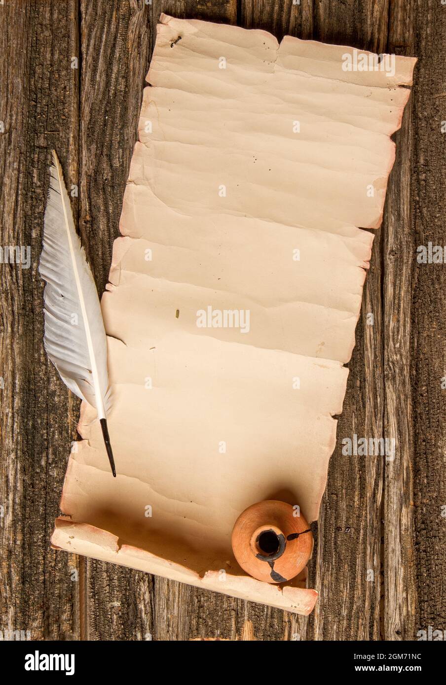 scroll of paper with place for text pen for writing and inkwell on rough wooden table Stock Photo