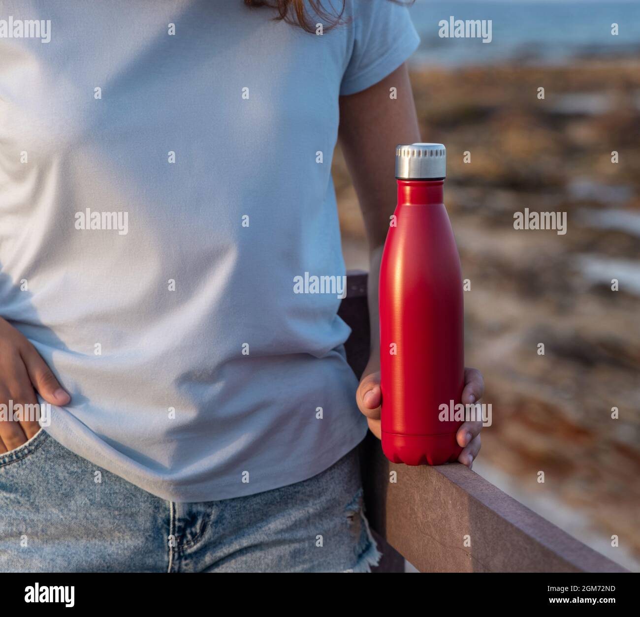 Teen girl in t-shirt standing and holding reusable water bottle in