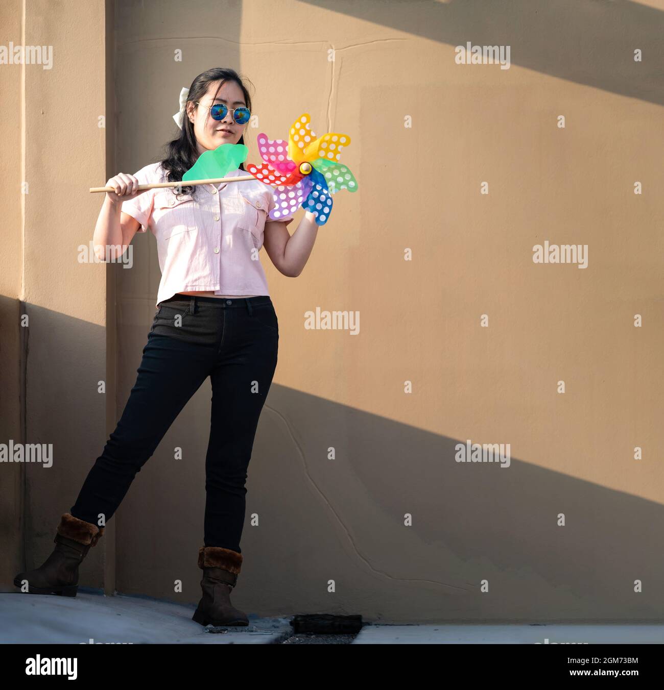 Asian woman posts and play Windmill Toy colourful rainbow colour on the building rooftop in sunset time. Stock Photo