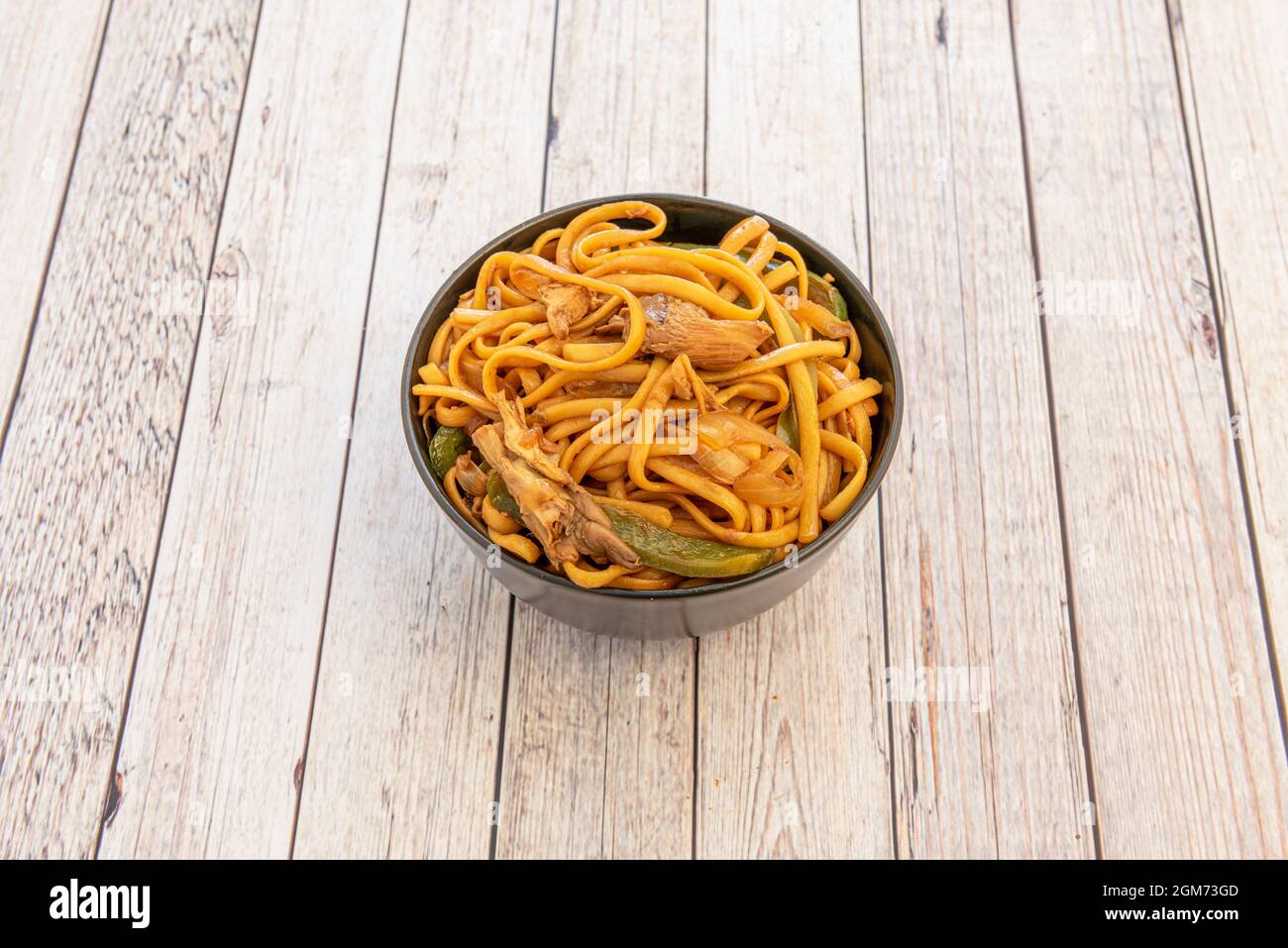 bowl of sauteed noodles with mushrooms, boletus and vegetables, peppers and onions with soy sauce on wooden table Stock Photo