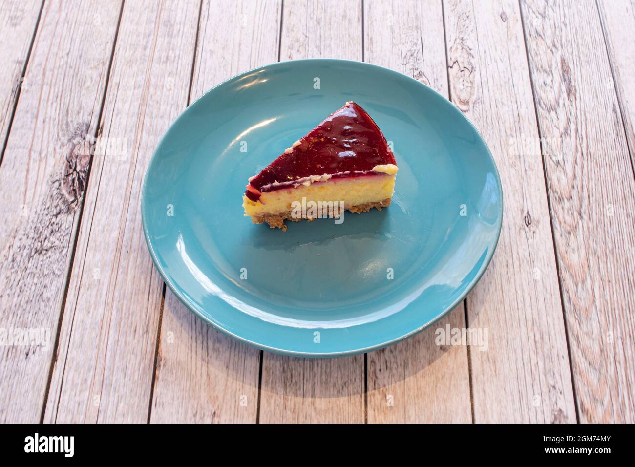 Small portion of industrially made cheesecake on plain blue plate Stock Photo