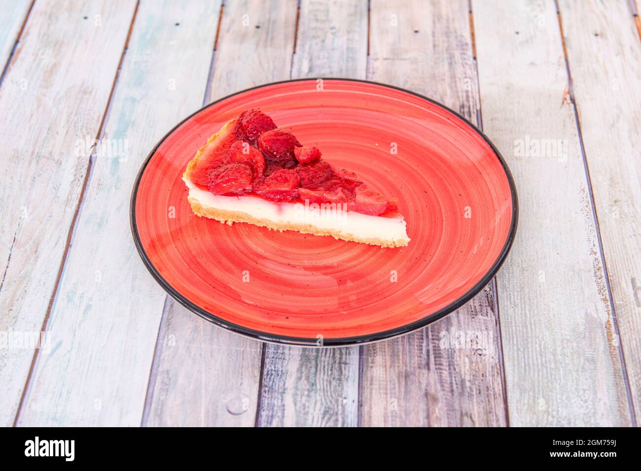 Portion of lemon and strawberry tart on red plate and wooden table Stock Photo