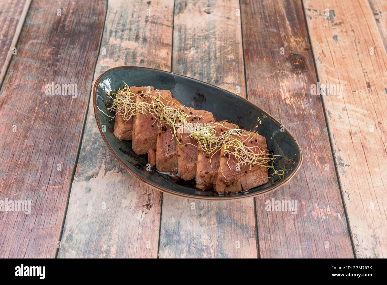 Portion of red tuna tataki with sprouted soybean sprout on a blue bowl and a meat table Stock Photo
