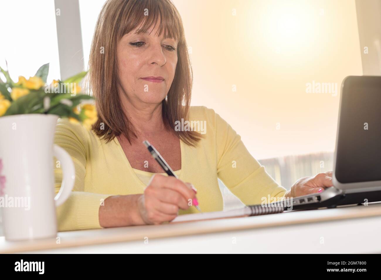 Mature woman taking notes and working on laptop, light effect Stock ...