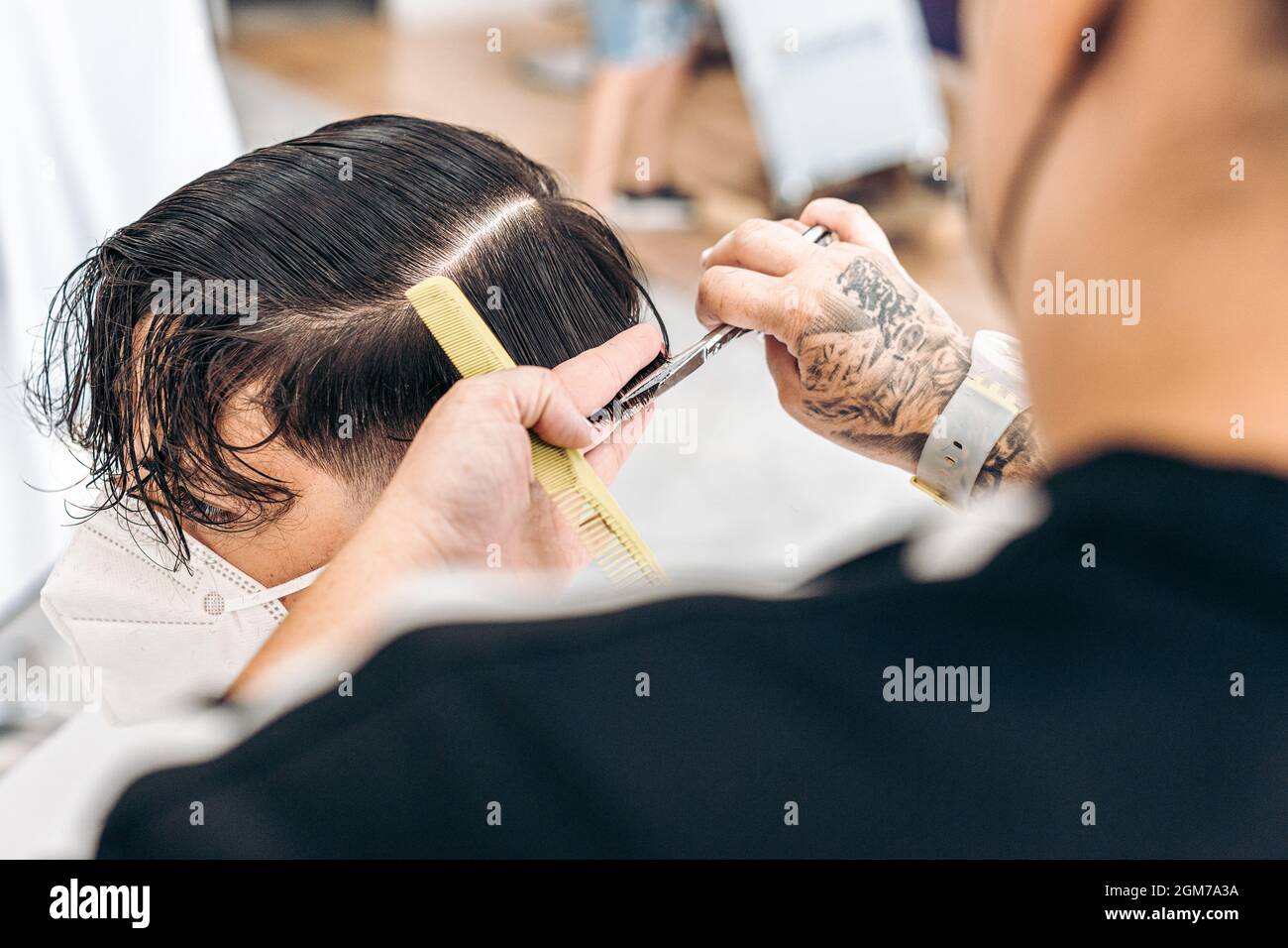 Hairdresser using scissors to cut the hair of a man with mask in a salon Stock Photo