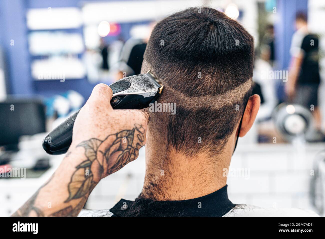 Barber shaving the back of the head of a man with an electric machine in a salon Stock Photo
