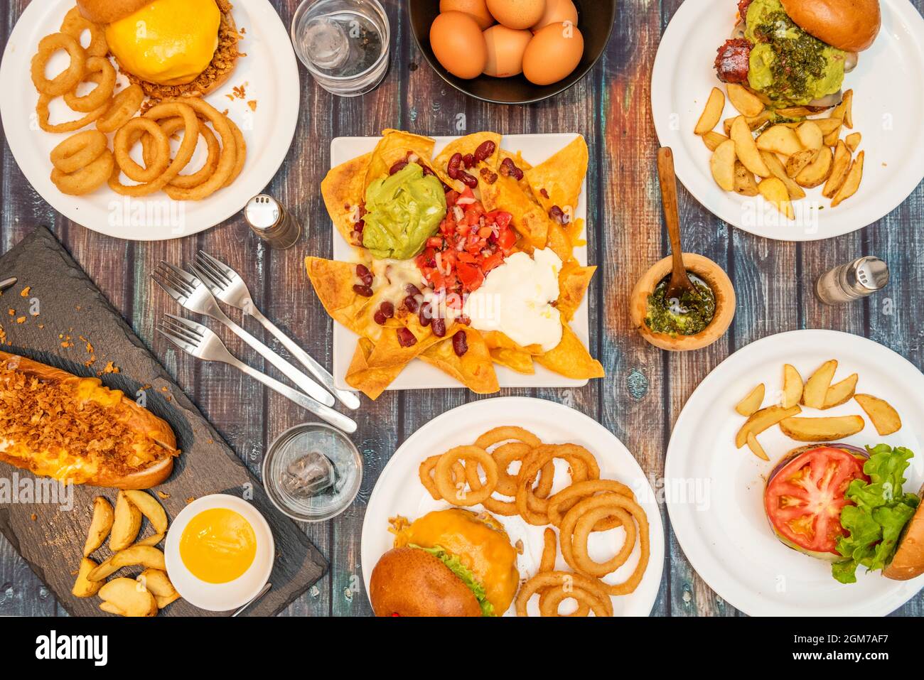 Unhealthy take away food set, hamburgers and hot dogs, battered onion rings, forks and glasses of water. Stock Photo