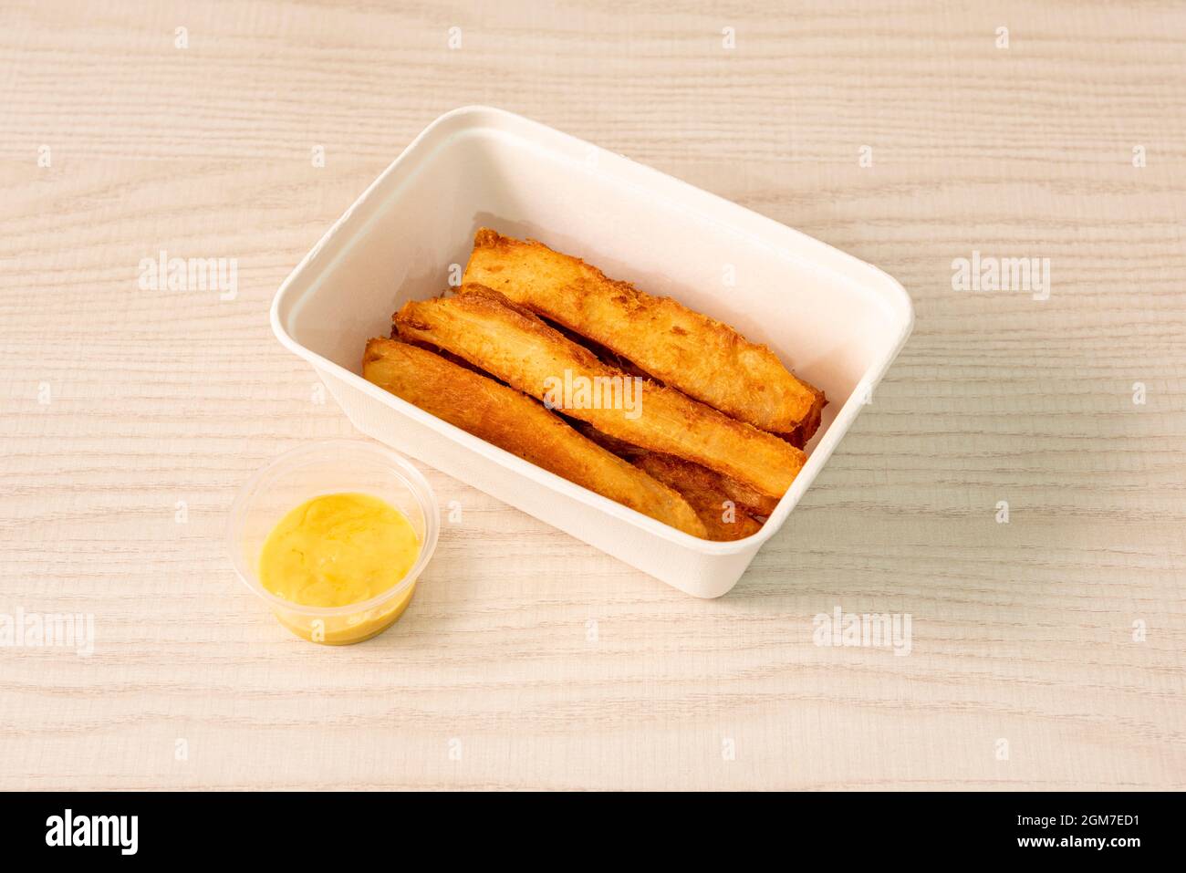 Fried cassava strips in a home delivery container with sweet curry sauce Stock Photo