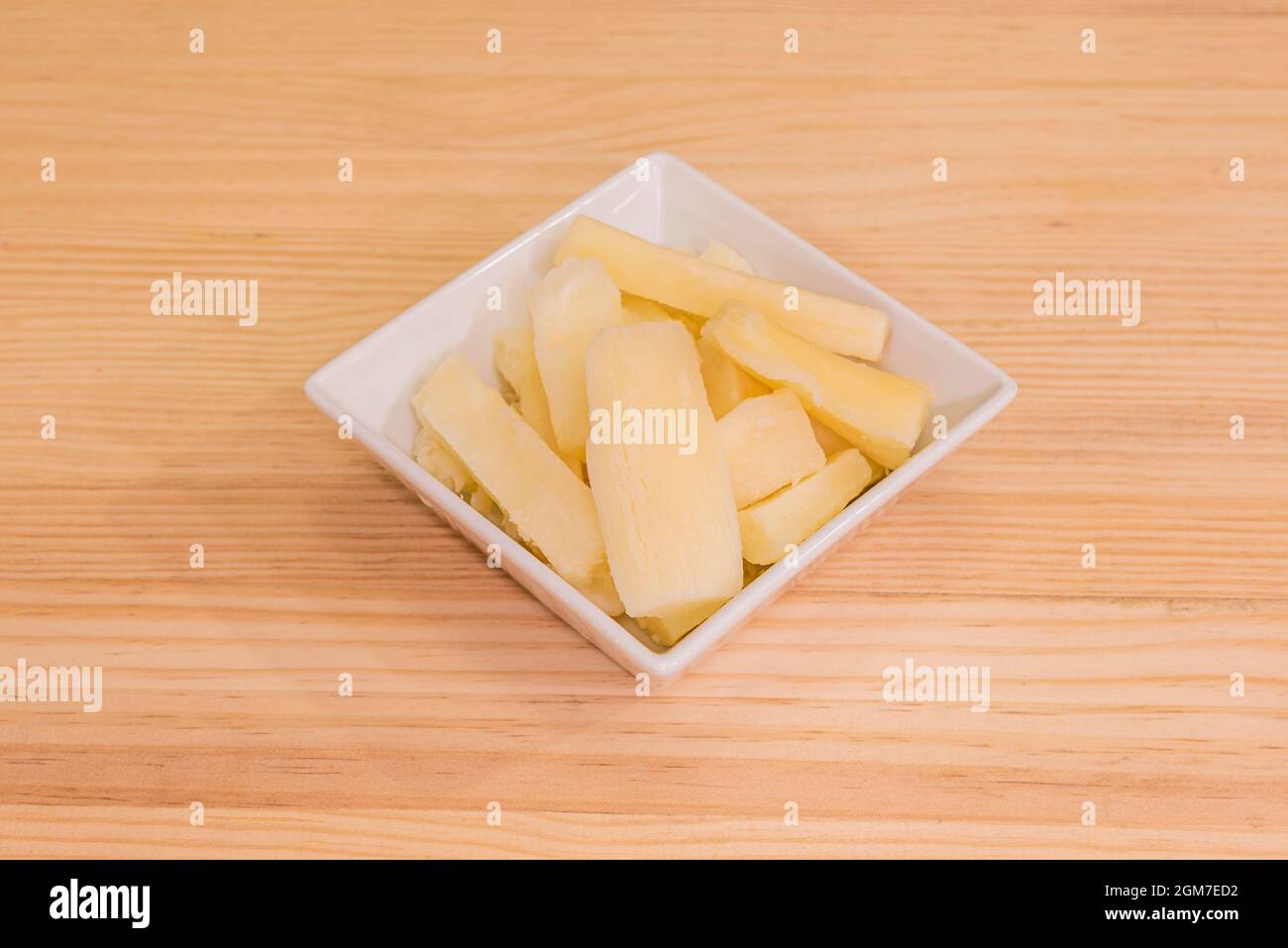 white square bowl filled with fried yucca pieces on wooden table Stock Photo