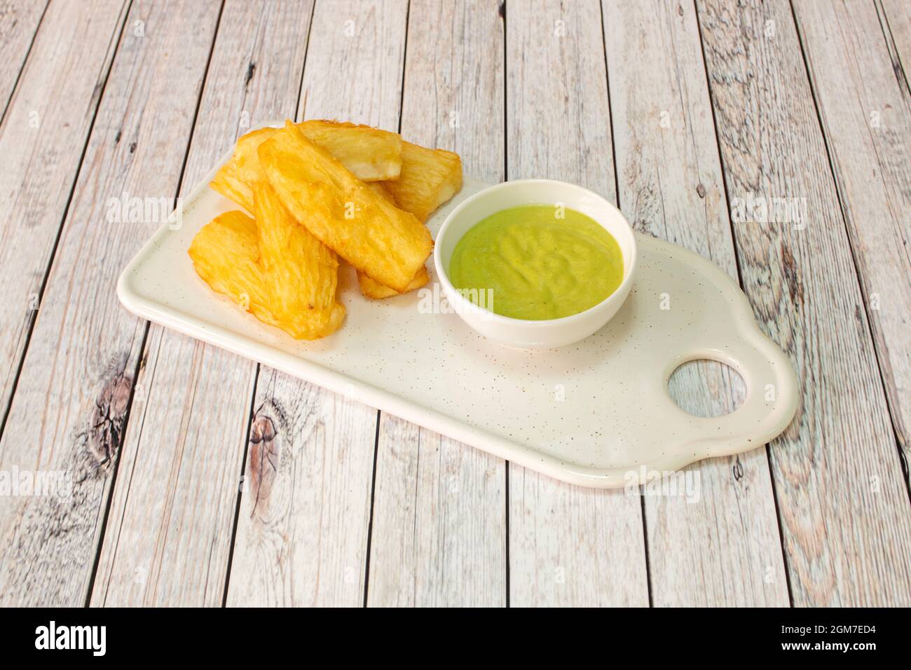 Tray of delicious fried yucca with green sauce to dip in a small white bowl Stock Photo