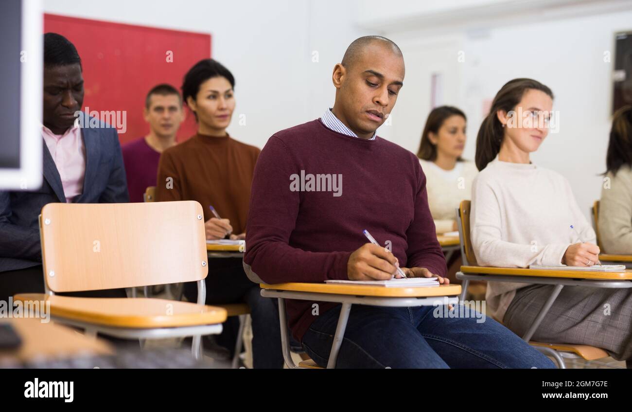 Multiethnic group of adult people studying together at tables . Focus on Latin American man Stock Photo