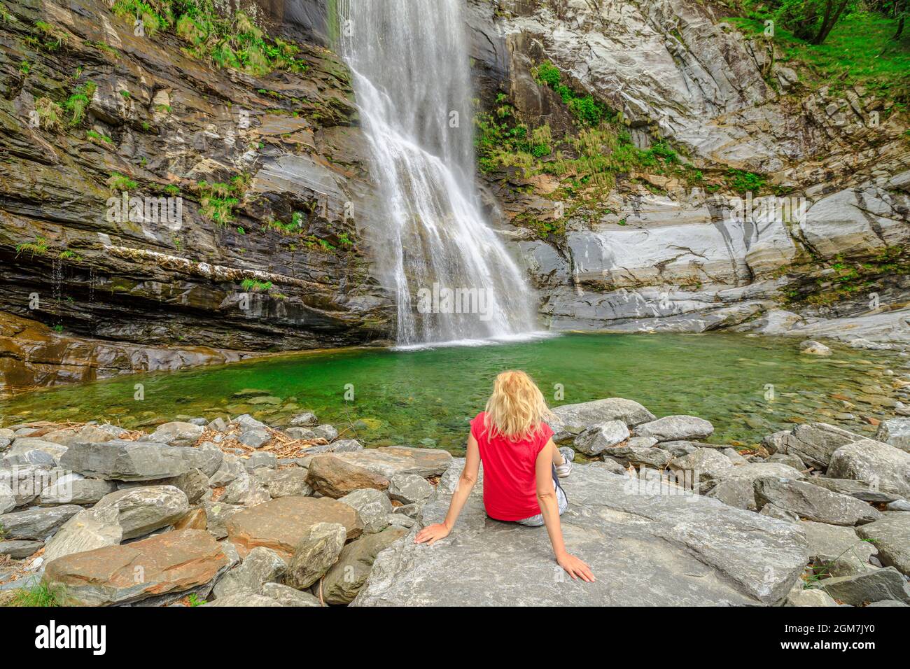 Woman sitting by the water of great waterfall of Bignasco, Valle Maggia, intersection point between the Bavona valley and Lavizzara valley, Cevio in Stock Photo