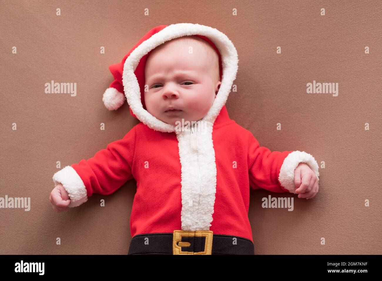 Newborn girl dressed in santa claus costume looking at camera with confused face. Stock Photo