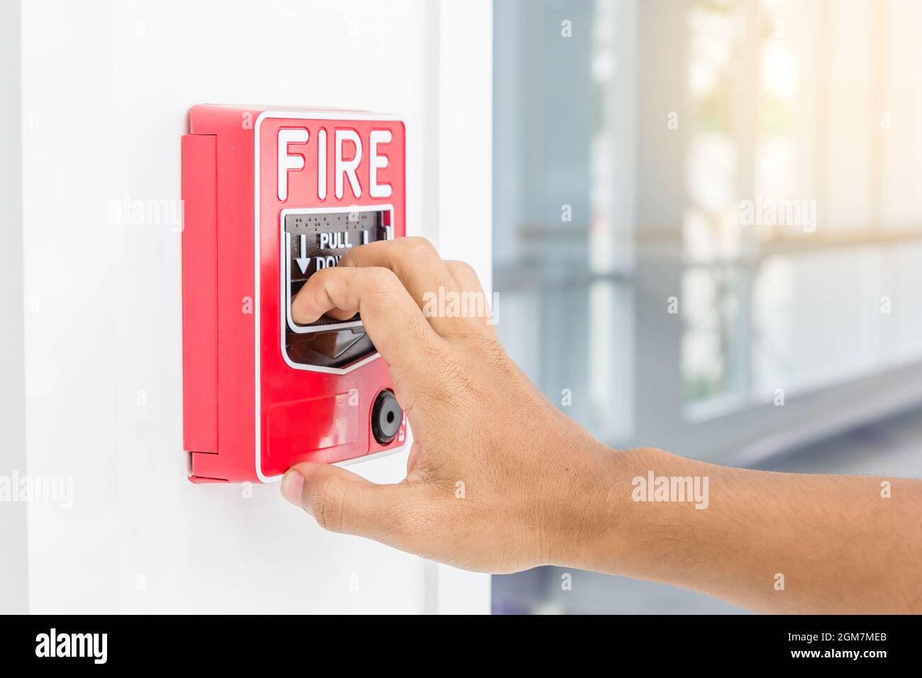 Hand of man pulling fire alarm switch on the white wall as background
