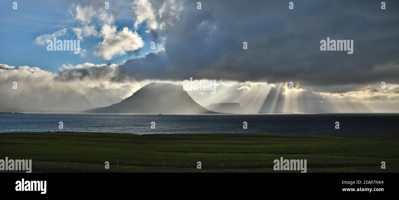 Sunrays shining on Kirkjufell mountain while a fishing boat sets its sails Stock Photo