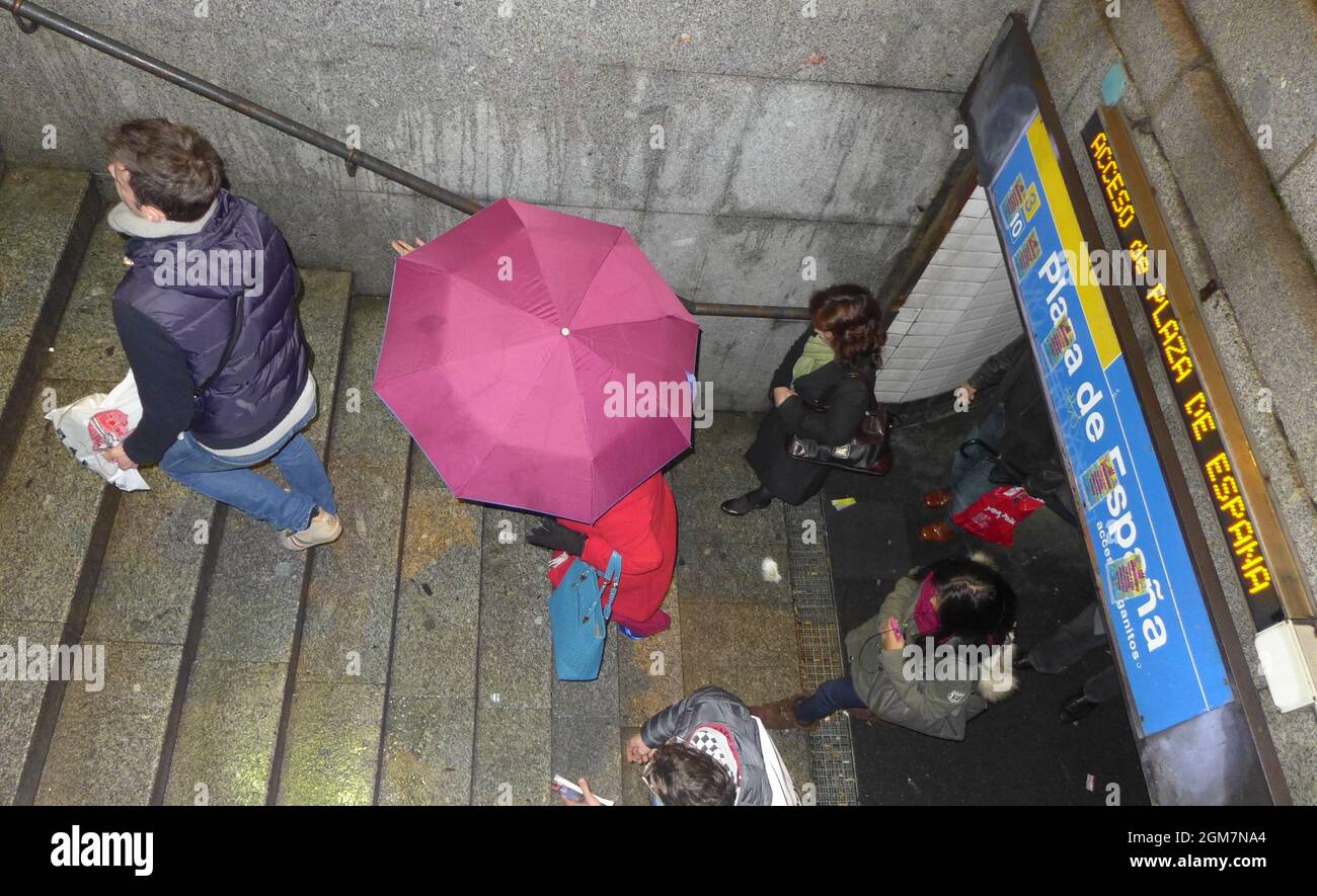People leaving metro station Plaza de Espana in Madrid during rain pink umbrella Stock Photo