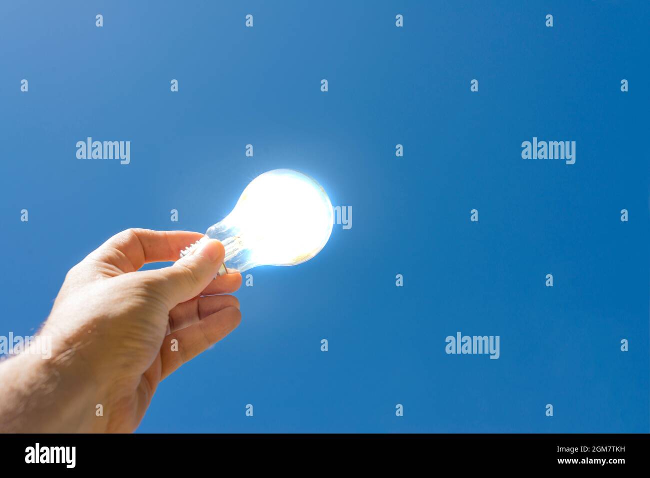 Hand holding a lit bulb with a blue sky in the background. Clean energy concept. Stock Photo