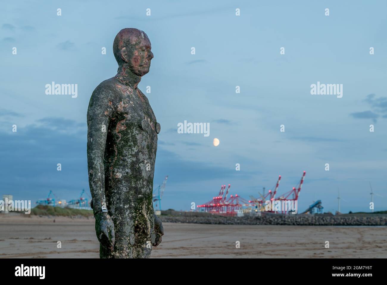 The moon rises over an Iron Man and Seaforth Docks on Crosby beach near Liverpool in September 2021. Stock Photo