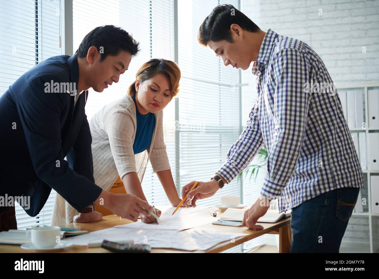 Team of serious business people bending over office table when discussing many charts and documents with marketing statistics Stock Photo