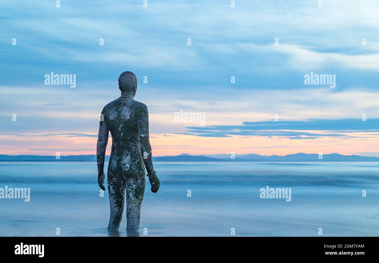 An Iron Man statue stands in water as the tide rushes in at sunset in September 2021 off Crosby beach near Liverpool. Stock Photo