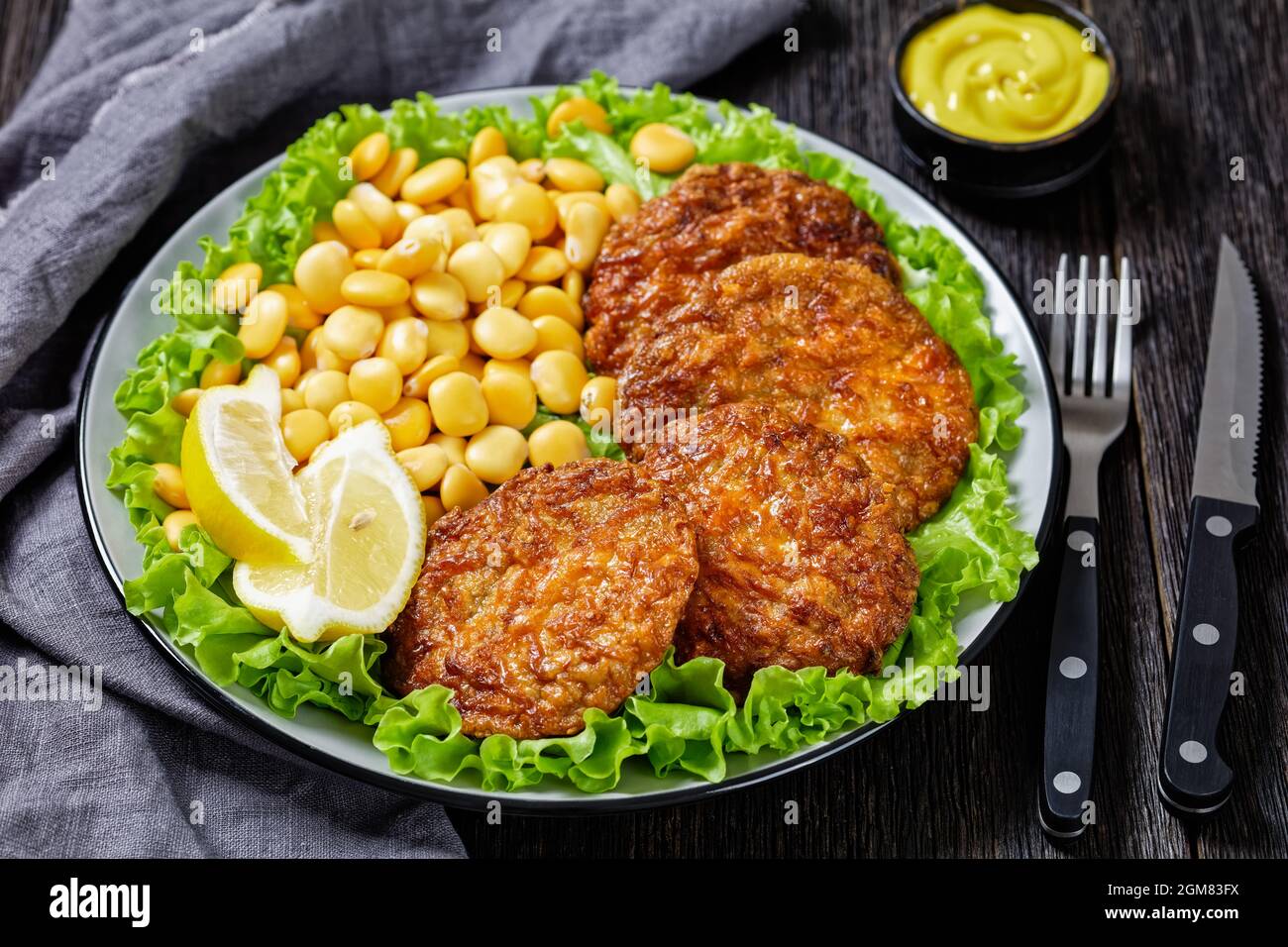 baked pork patties with browned cheese crust on a green lettuce lives with  lupin beans, ketchup and mustard on a plate Stock Photo