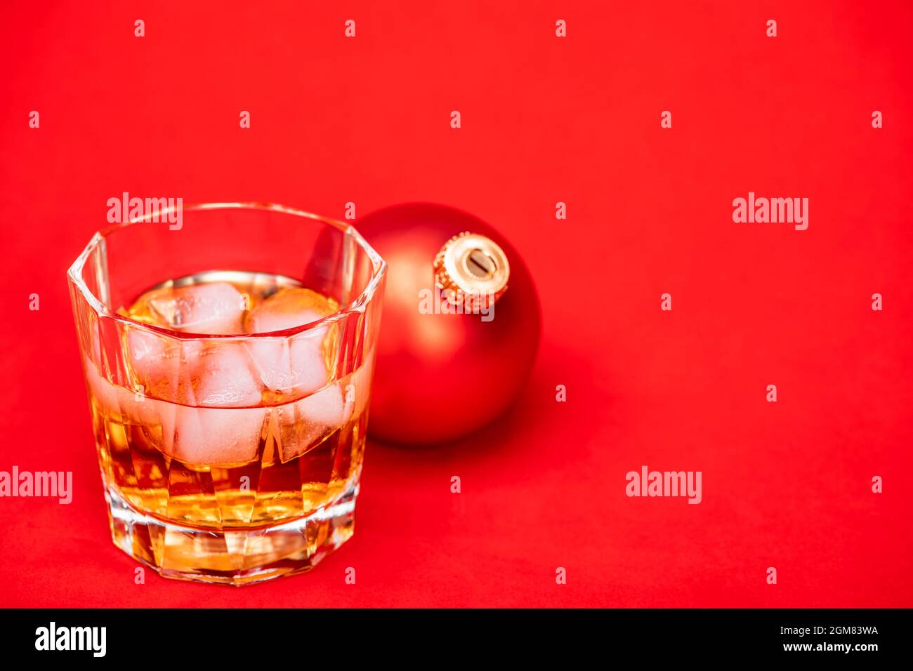 Glass of whiskey with ice cubes and christmas bauble on red background - christmas drink concept Stock Photo