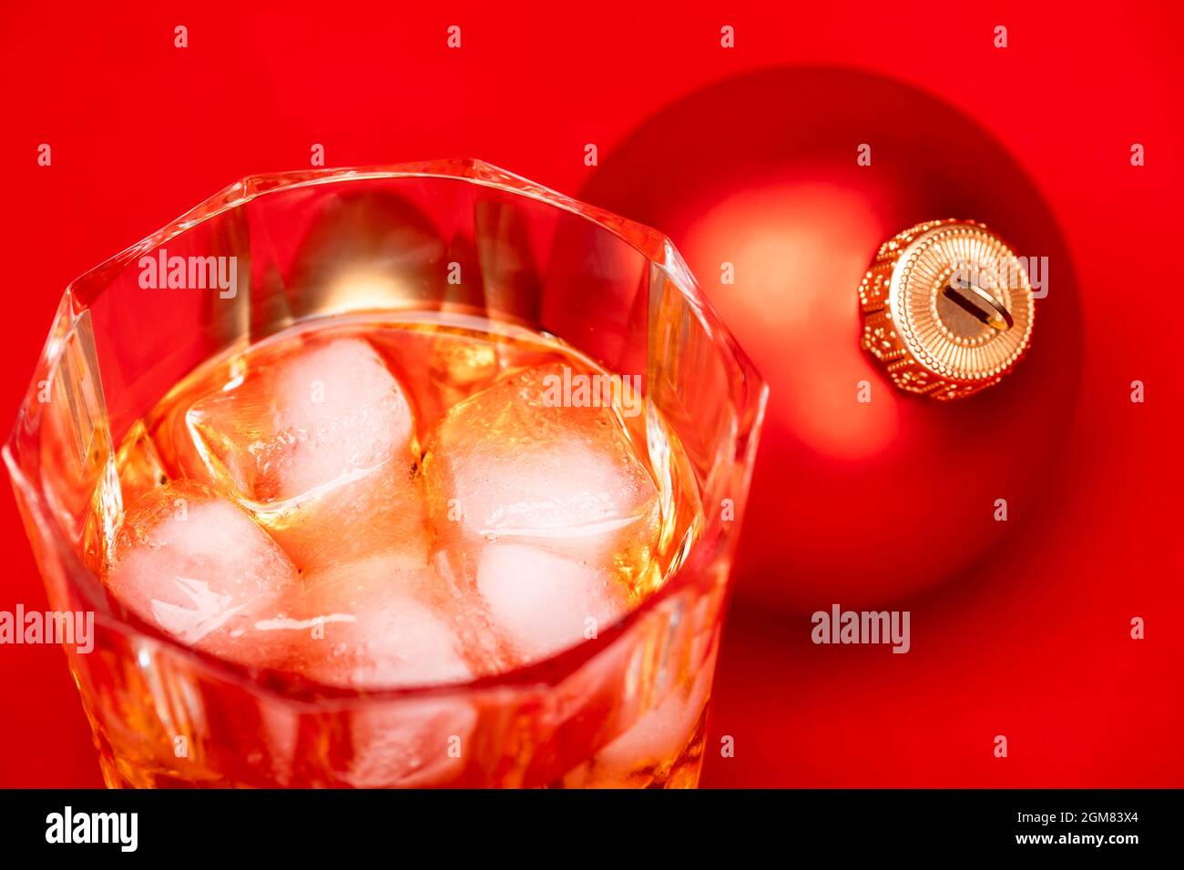 Glass of whiskey with ice cubes and christmas bauble on red background - christmas drink concept Stock Photo