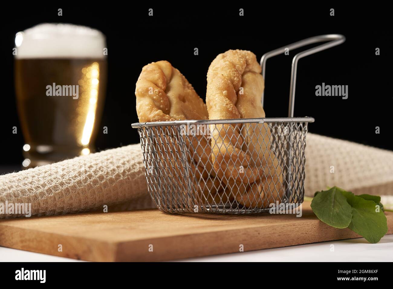 Empanadas inside deep fryer with glass of beer in the background Stock