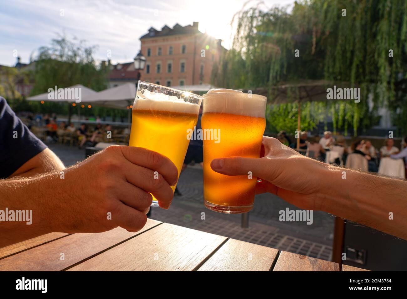 friends cheers toast with two beers in summer sunshine in Ljubljana outdoor pub Stock Photo