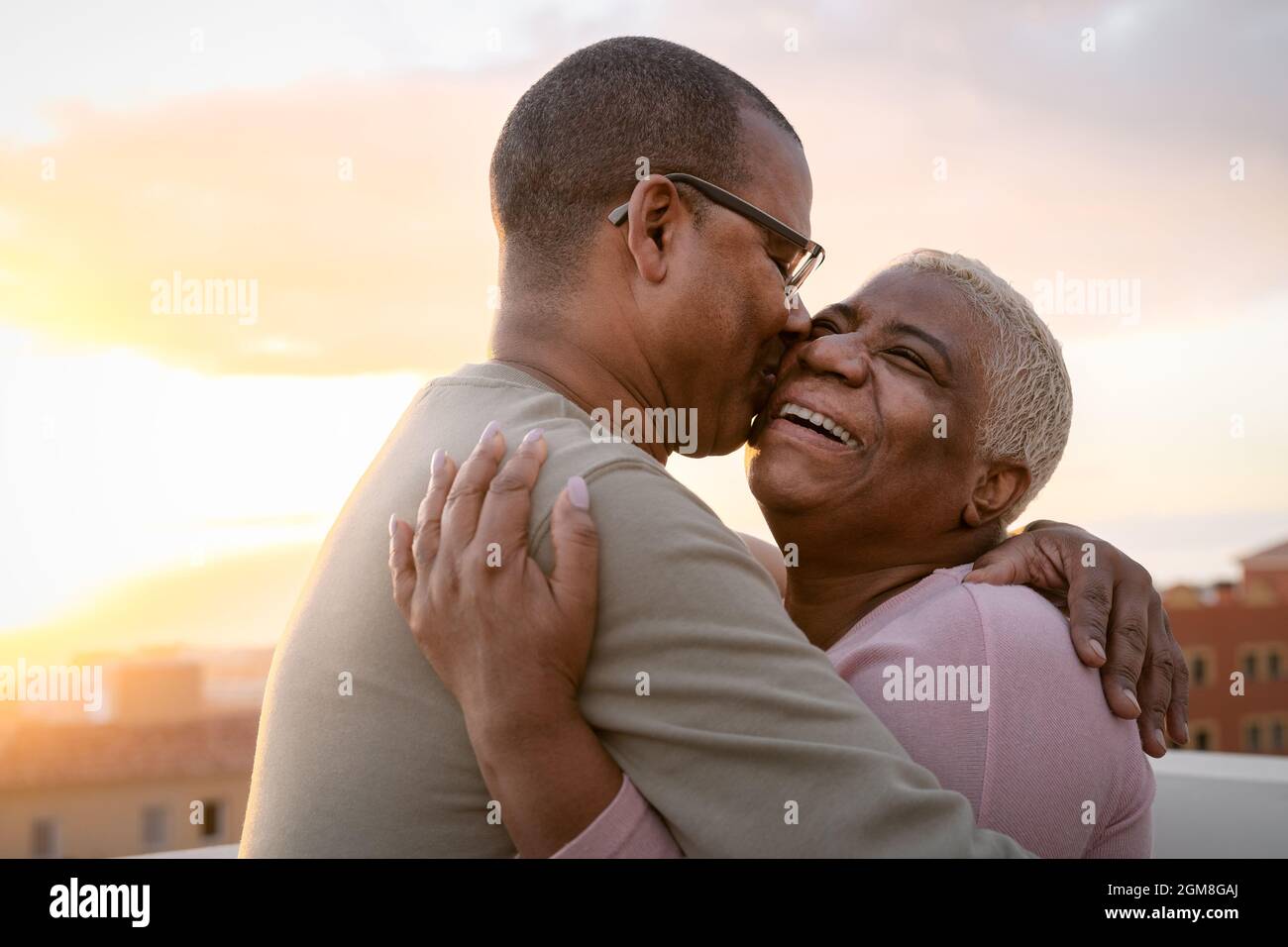 Happy Latin senior couple having romantic moment embracing on rooftop during sunset time - Elderly people love concept Stock Photo