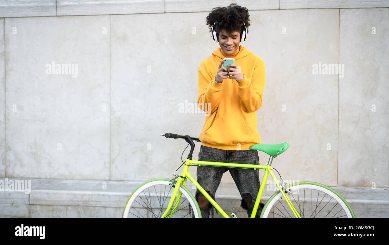 Happy African man using mobile smartphone outdoor while riding with bike in the city - Youth millennial generation lifestyle and technology concept Stock Photo