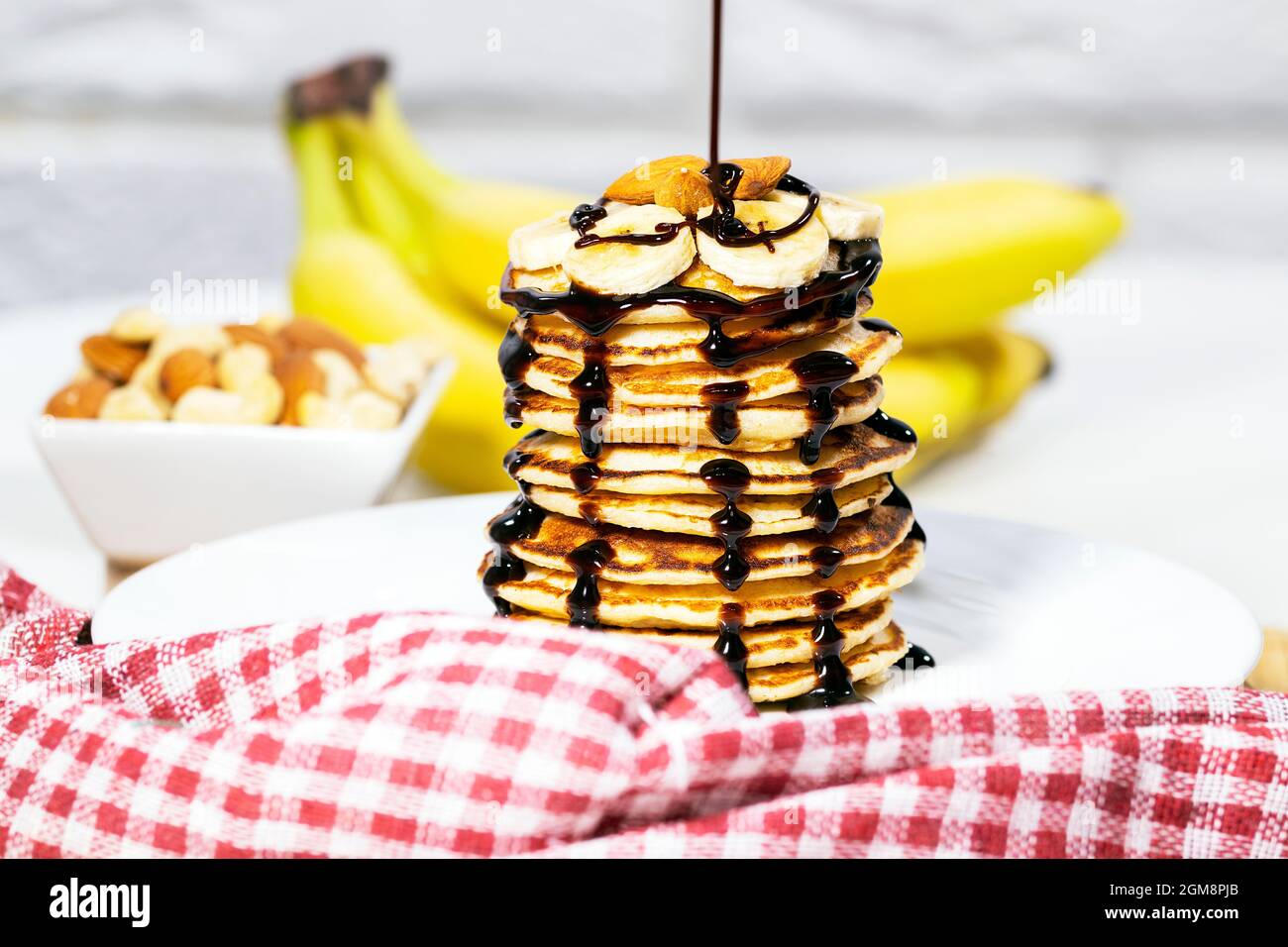 Pancakes with Chocolate Syrup, Nuts and Bananas. Stack of whole flapjack. Chocolate Being Poured Into Slapjack, Tasty breakfast and Healthy Food Stock Photo