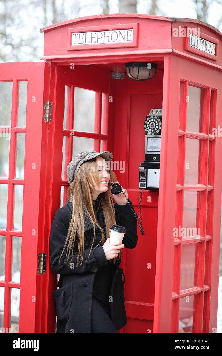 Beautiful young girl in a phone booth. The girl is talking on the phone from the payphone. English telephone booth in the street and a woman talking o Stock Photo