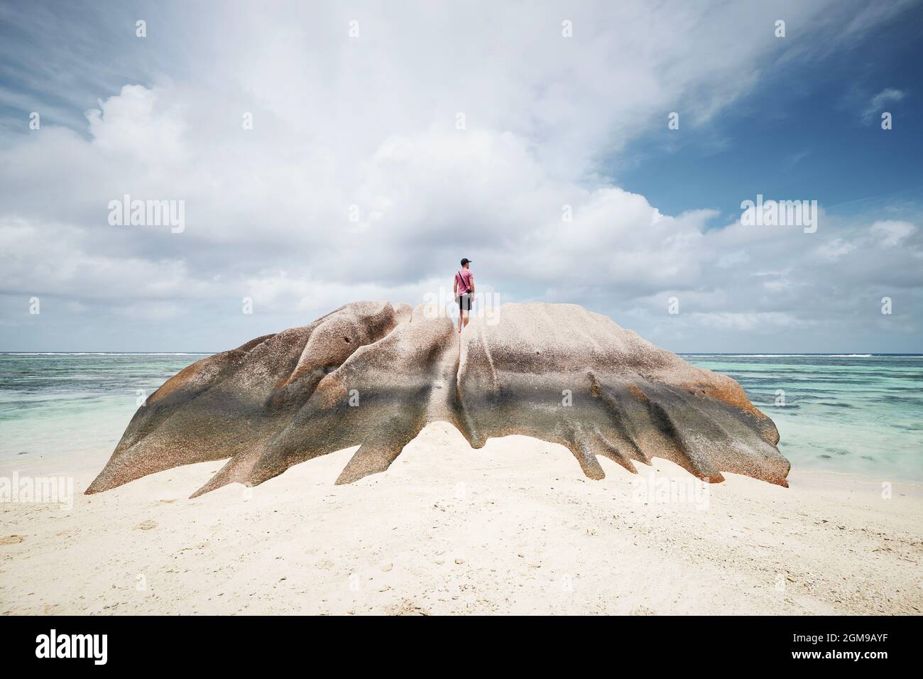 Man standing on rock and looking at view. Lonely tourist enjoying calm on idyllic beach in Seychelles Stock Photo
