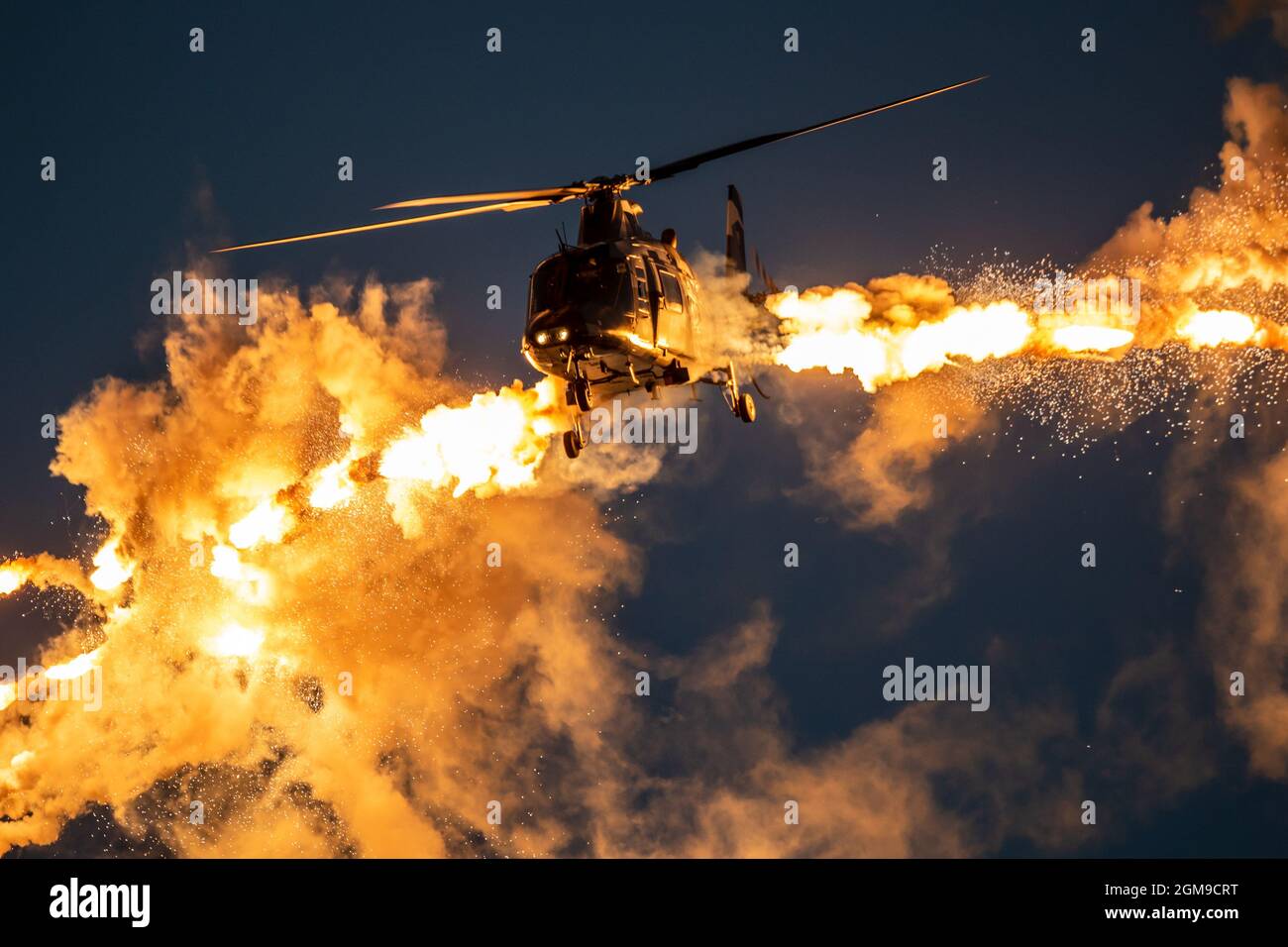 Army helicopter in flight firing off defensive flare decoys at dusk. Stock Photo