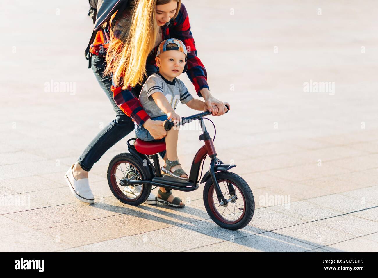 Little happy child learns to ride a bike with her mom in the park in the park Happy young mom teaches her son to ride a bike in the park on a