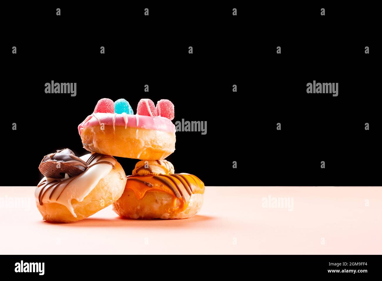 Photograph of 3 donuts decorated with jelly beans and drawn with chocolate.The photo is taken in horizontal format on a cream colored cardboard and a Stock Photo
