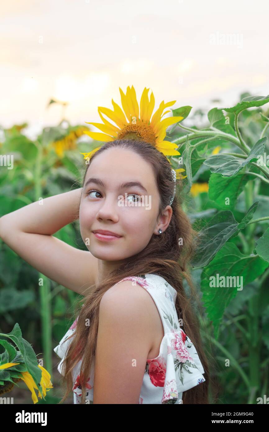 Beautiful teen girl is smiling with sunflower in summer field Stock Photo