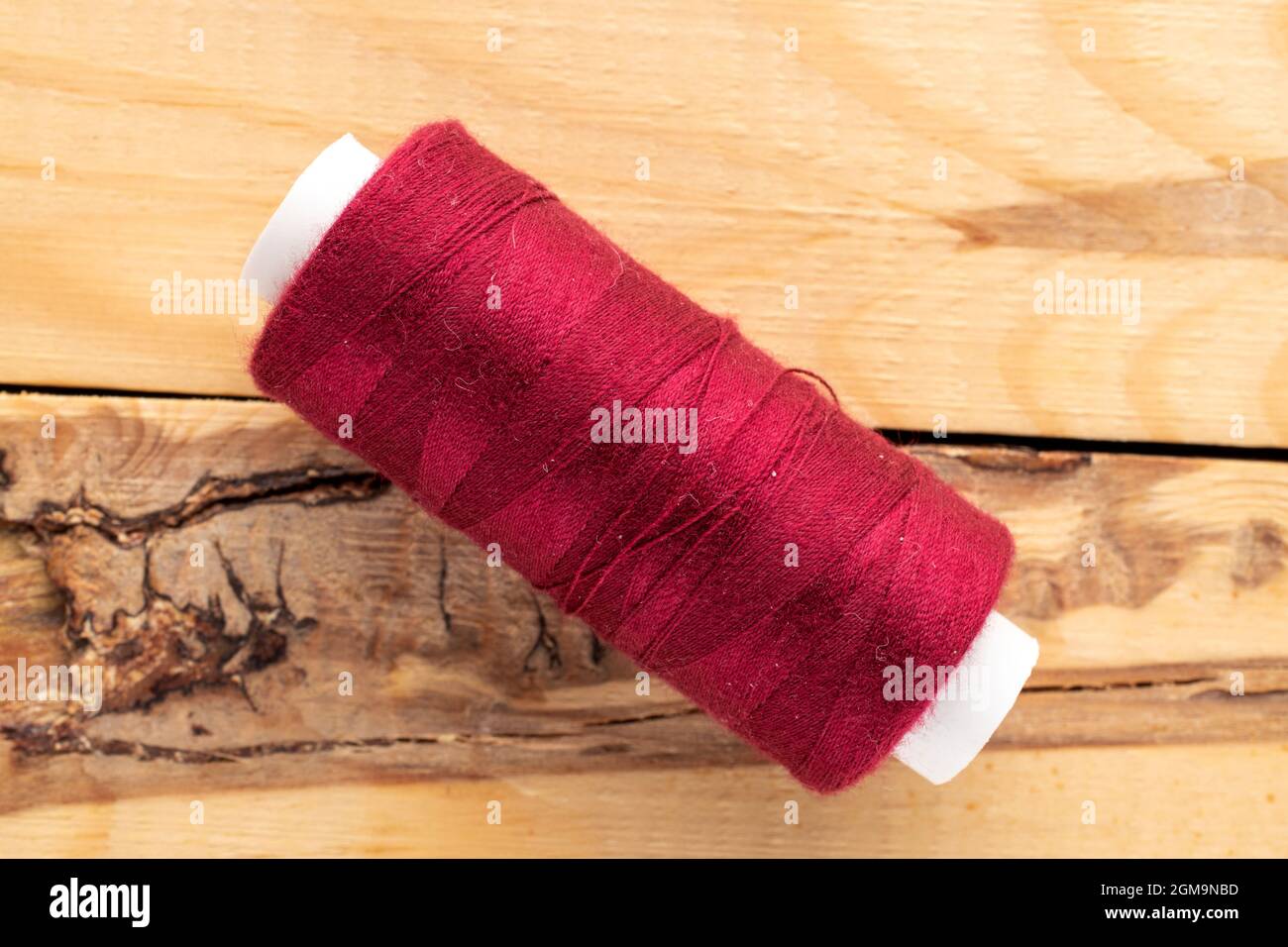 One spool of burgundy thread, close-up, on a wooden table, top view. Stock Photo