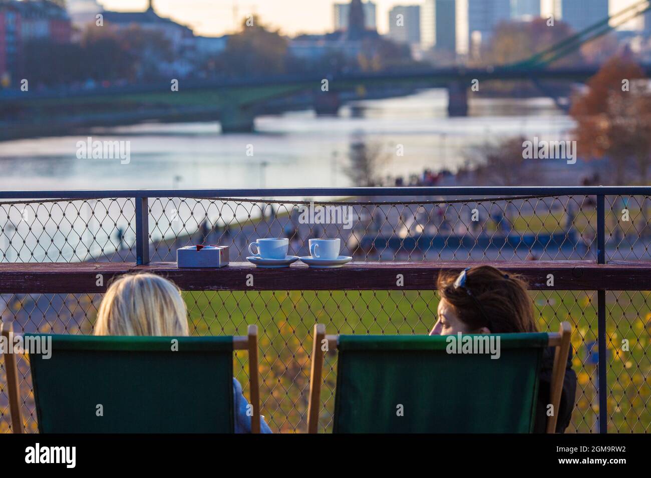 Two woman dinking coffee and sitting on the rooftop of restaurant Oosten, looking over the park and promenade at River Main, in the background the sky Stock Photo
