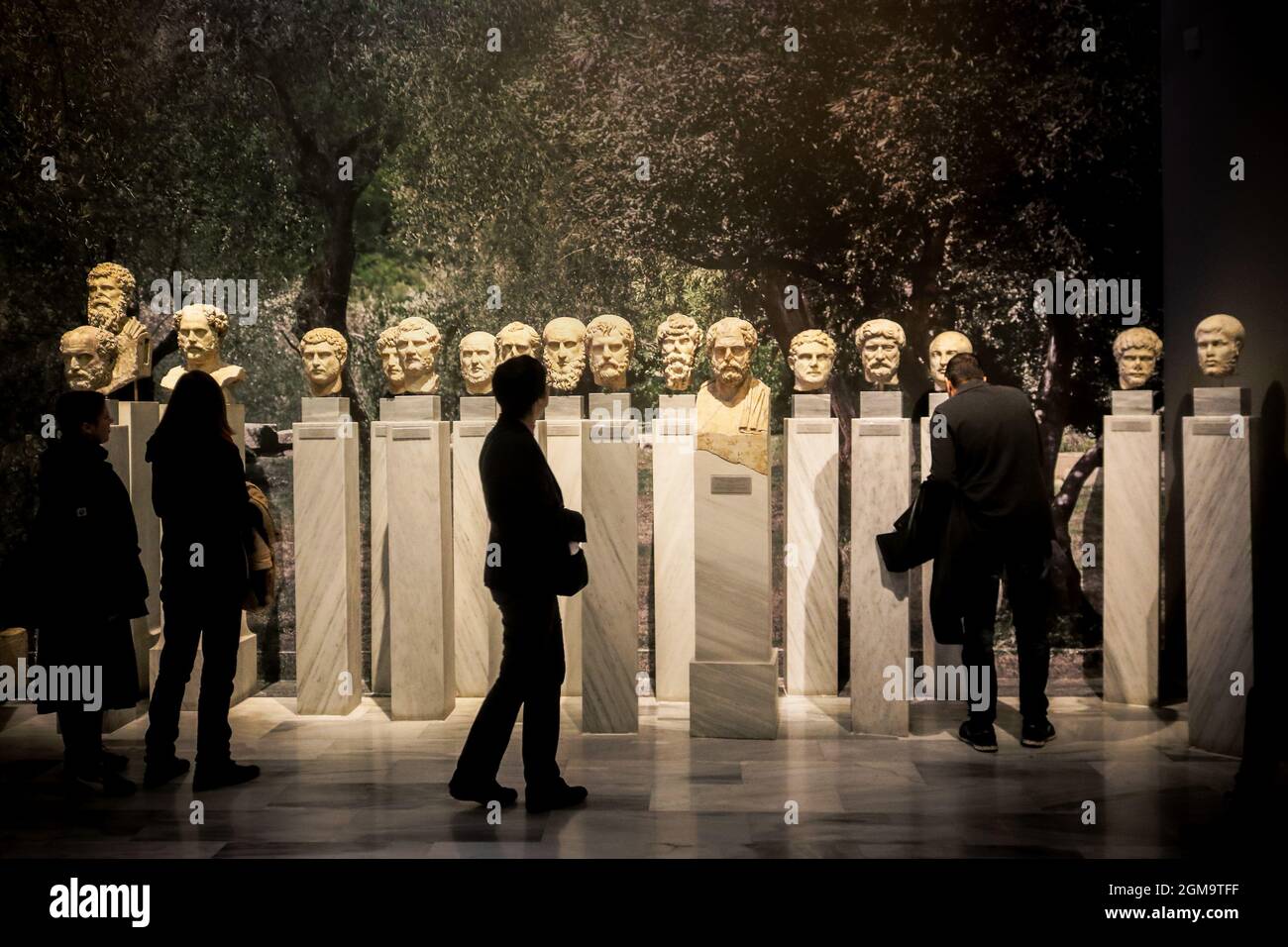 01-04-2018 Athens Greece - Shadowy people walking past heads of Greek philosophers on pedestals with garden background Stock Photo